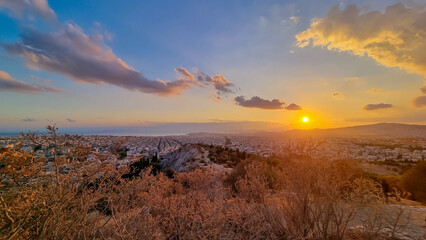 Fototapeta premium Panoramic view during sunset of the city of Athens seen from Filopappou Hill (hill of muses), Athens, Attica, Greece, Europe. Athens cityscape and Aegean sea. Beautiful sunset point with aerial view