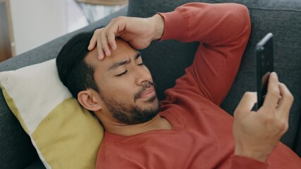 Stress, depression and man with phone on couch or sofa in living room at home reading bad news, breakup text or problem. Confused, mental health and anxiety of sad depressed male on mobile app tech.
