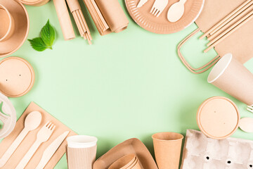 Frame made with paper utensils, food containers, paper drinking straws, cups, sheets of parchment over light green background with copy space. Sustainable food packaging concept