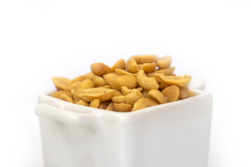 Closeup of roasted salted peanuts in a white square bowl.  Isolated against a white background.