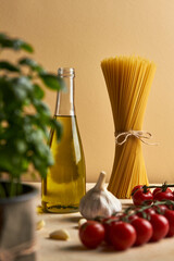 Food background, healthy mediterranean concept of
organic ingredients.
Still life with olive oil,tomato,garlic,basil leaves and raw pasta on beige background. Top wiev with copy space