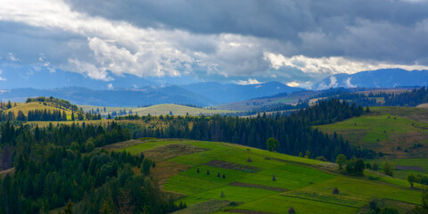 Obraz premium mountainous countryside landscape in september. rural fields and forest on the hills rolling in to the distant ridge. wonderful nature scenery on a cloudy weather day in dappled light