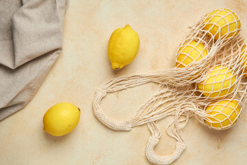 Fresh citrus in mesh bag on beige background. Lemons and limes in string shopping bag with tonic...