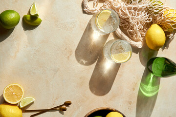 Fresh citrus in mesh bag and glasses of lemon water on beige background. Lemons and limes in string...
