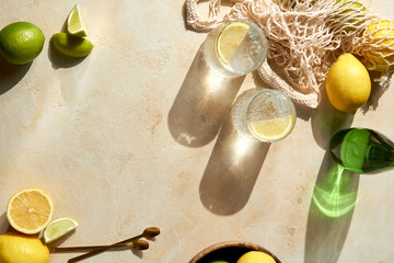 Fresh citrus in mesh bag and glasses of lemon water on beige background. Lemons and limes in string...