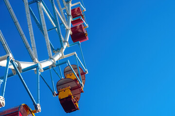 against the background of a blue sky, an amusement park, ferris wheel cabins, view from below, copy space