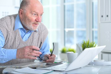 Emotional senior man reading newspaper at home