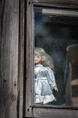 Scary doll looks out the window of an old house. Creepy girl doll in a window