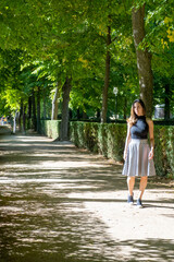 Fototapeta premium Summer sunny lifestyle fashion portrait of young woman walking in a park using striped skirt and black blouse