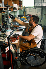 Fototapeta na wymiar A workshop owner in a wheelchair reaching for tools on a shelf.
