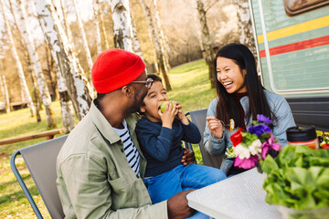 A family has healthy lunch together in nature in front of the van.