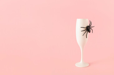 Creative idea made of champagne glass with spider on pastel pink background. Minimal Halloween party concept. Copy space.