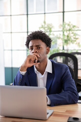 Portrait of skeptical male office worker. Serious businessman at desk looking at camera, covering mouth with hand. Business, office work concept.