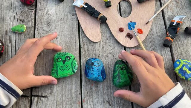 A child plays with pebbles painted with acrylic paints. Home hobbies are authentic. Artwork on stones.
