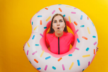 Beautiful young woman in a stylish pink swimsuit with a donut inflatable ring on a yellow background