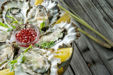 Large fresh oysters with sweet dipping sauce and lemons on a plate of crushed ice.