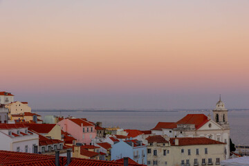 Fototapeta na wymiar Typical cityscape of Lisbon, Sunset in the evening with orange brick roof top of buildings and housing with harbor view, Narrow houses between small street in coastal of atlantic, Lisbon, Portugal.