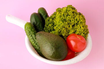 Fresh vegetables  in sieve colander on pink color background. Cucumber tomato avocado salat. Healthy food concept background. Vegan vegetarian food diet clean eating