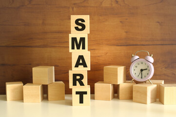 Five wooden cubes stacked vertically on a brown background make up the word SMART.