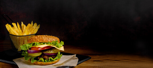 Delicious burger and french fries. Banner, billboard. Dark background. Vintage.