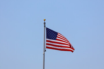 An American flag  on a pole flying on the blue sky.