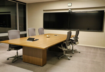 An empty conference room with two large screens on the wall and a view of a window at night.