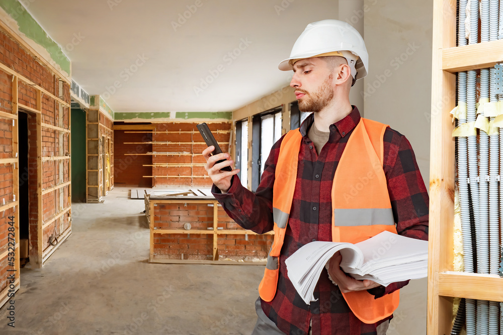 Poster builder man. worker with phone and documentation. man stands in unfinished building. builder next to