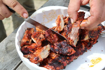 a man cuts pork ribs on the grill with a knife during a picnic