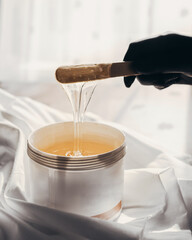 Liquid yellow sugar paste or wax for depilation on a stick close-up hands in black gloves