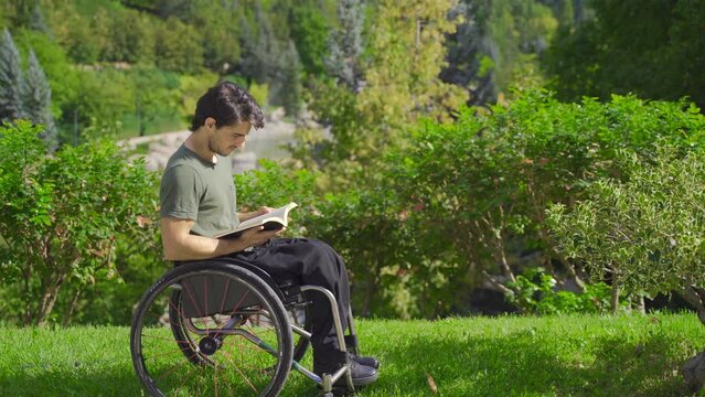 Disabled teenager in a wheelchair reading a book in a nature park.
Young man sitting in his wheelchair among the trees reading a book.
