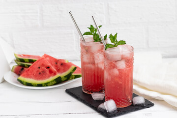 Watermelon smoothie or iced juice with watermelon slices and mint leaf on a white wooden background