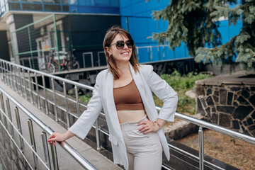 Beautiful business woman in white suit and sunglasses during break standing near modern office building