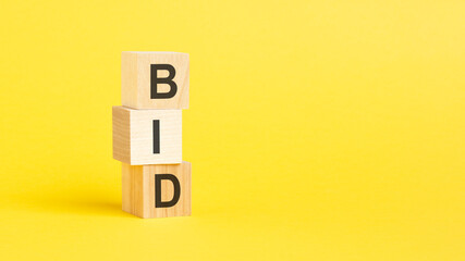 BID - text on wooden cubes, on yellow background