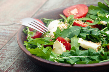 Green salad made with arugula, tomatoes, cheese mozzarella balls and sesame on plate