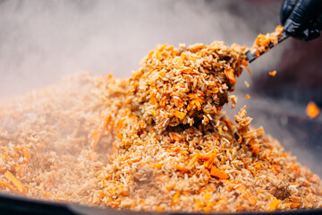 Chef cook prepares Yellow pilaf in cauldron with beef from street food market at festival