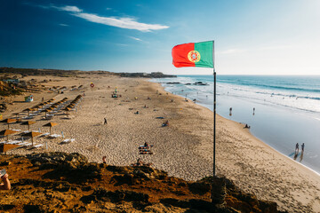 Portuguese flag waving over blue sky and ocean, Guincho Beach, Portugal