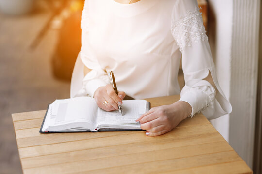 Close-up of a business woman hand writing notes on notepad, making agenda on personal organizer, year 2023 calendar on table in cafe and morning sunlight, work and event planning