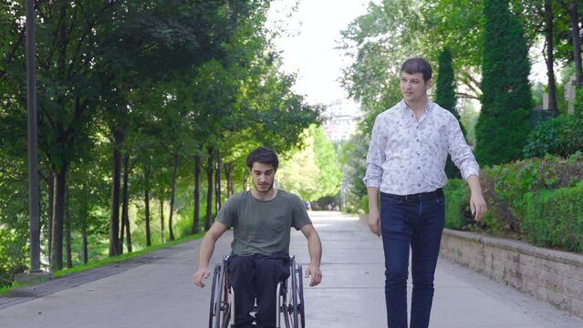 Disabled teenager is driving his wheelchair and talking to his friend walking next to him.
The two friends are walking on the street, chatting and talking.
