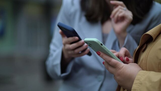 Close up focus on females hands using phones. Two women with smartphones on the street, the girl explains, shows, tells, demonstrates, gesticulates with her hand