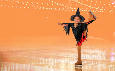 Little young skater posing in a witch costume for halloween on ice on an orange background with festive lights