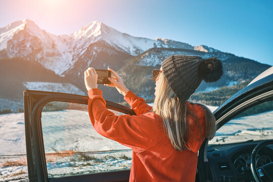 Woman travel exploring, enjoying the view of the mountains, landscape, lifestyle concept winter vacation outdoors. Female with mobile phone standing near the car in sunny day.
