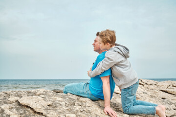 Happy family, father and son bonding, sitting on stone by the sea looking at view enjoying summer vacation. Togetherness Friendly concept