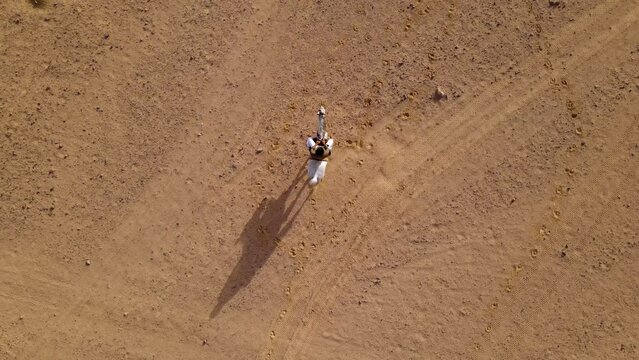 A following drone shot from the top of a man riding a white horse.