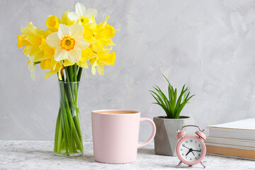 Design of woking table. Succulent plant, bouquet of daffodils, alarm clock, cup of coffee and books on the table. Morning concept. Minimal home design