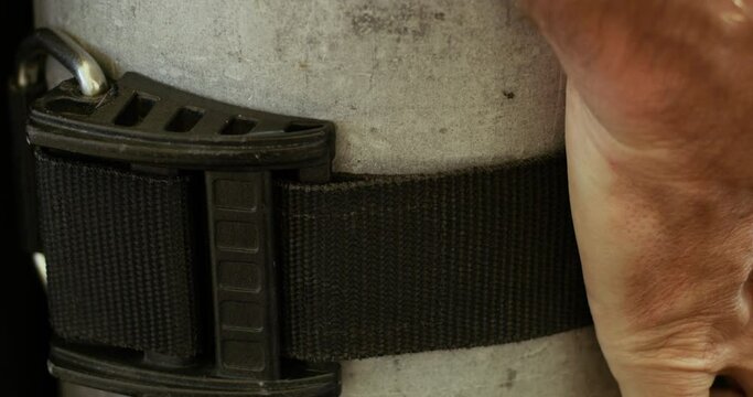Close shot of an arm strapping a black belt around an oxygen tank.