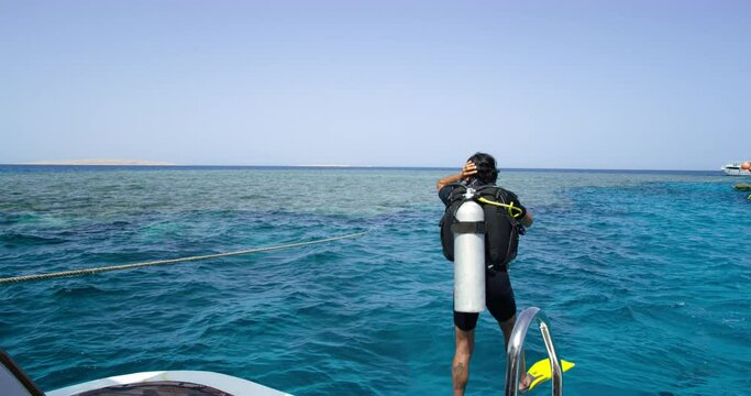 A male scuba diver is jumping into the ocean's water from a boat.