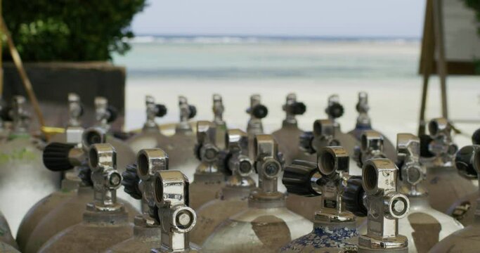 A steady shot of shiny oxygen tanks grouped on a beach.