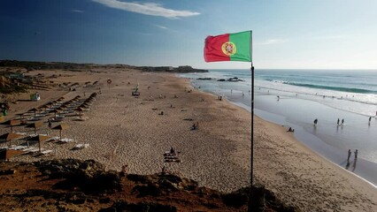 Portuguese flag waving next to sea on a summer day slowly revealing the beach in background in Guincho, Portugal - Powered by Adobe