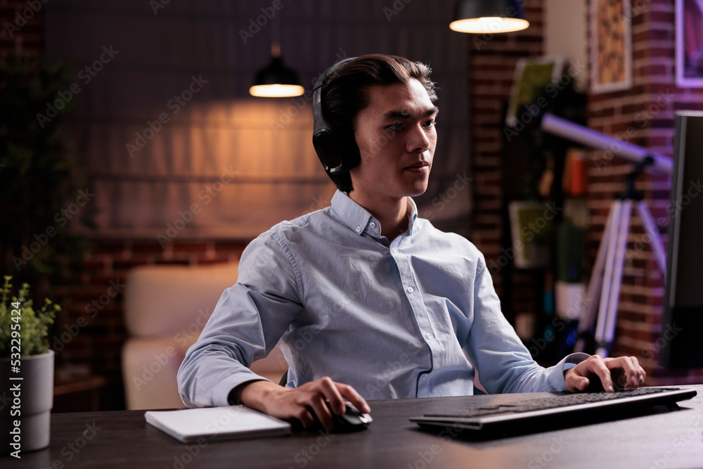 Poster office worker using headphones and working on computer at home, listening to podcast or show online.