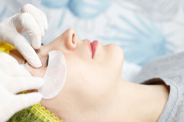 beautician is gluing a patch under eyes, before the procedure of eyelash extension. Artificial extended eyelashes